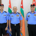 Three uniformed security officers pose for a formal photo in front of flags, with medals on their chests.