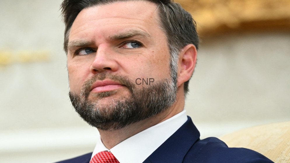 Close-up portrait of a man with a beard in a navy suit and red tie, looking to the left.