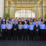 Group photo of uniformed officers in blue and gray uniforms with medals, and civilians in suits, posed outside a grand building entrance.