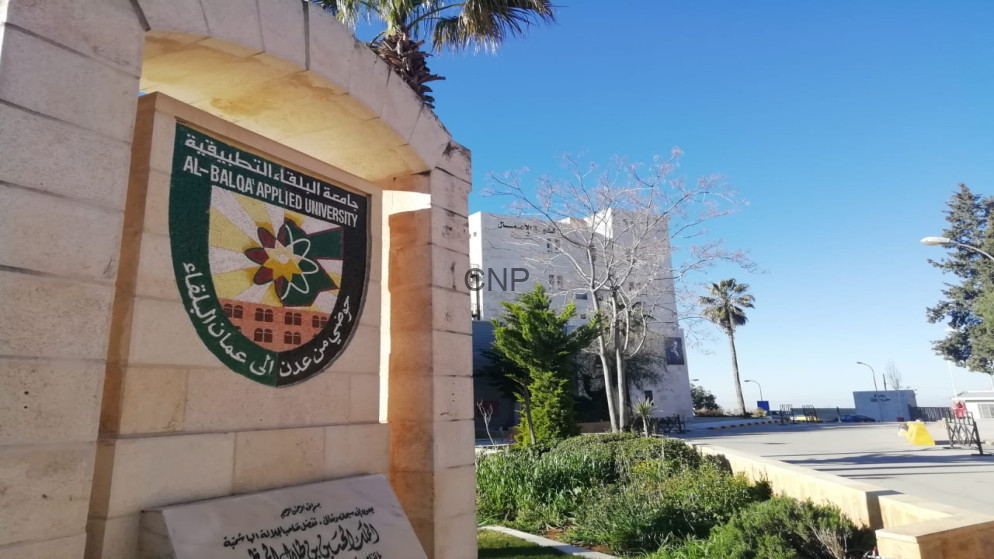 Stone arch and pillar show the Al-Balqa Applied University crest on campus, with trees and a clear blue sky.