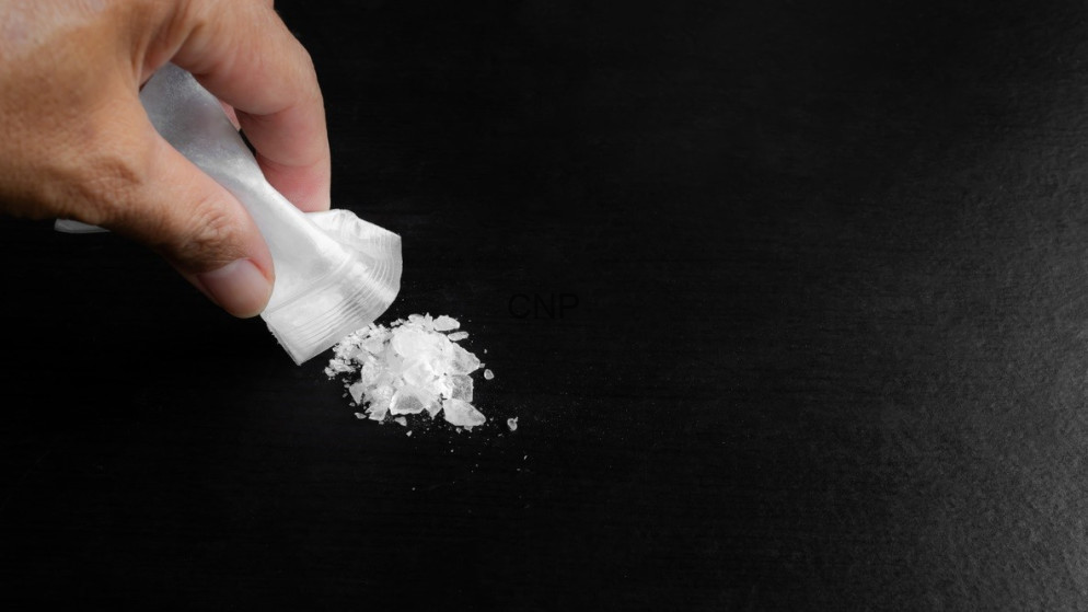 Close-up of a hand emptying white powder from a small packet onto a dark surface, on a black background.