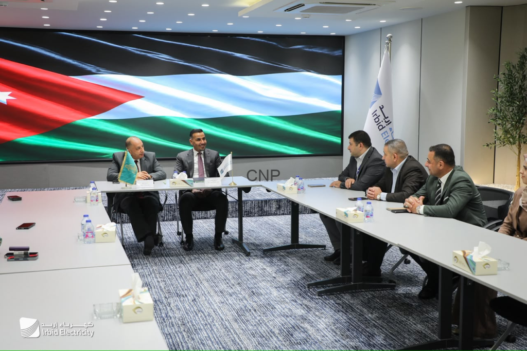 image - Center News Network Executive meeting at Irbid Electricity: six professionals in suits sit around a large conference table with a Jordan flag on the screen behind them.