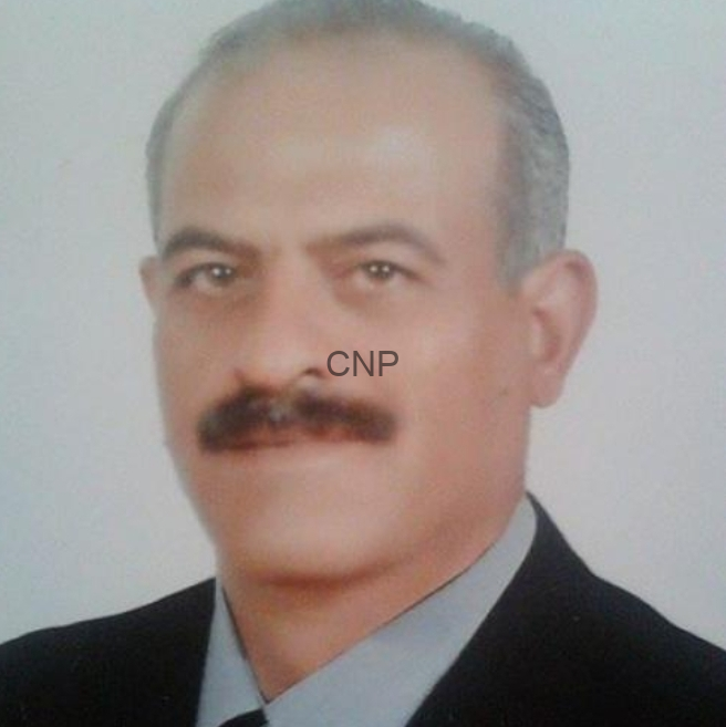 image - Center News Network Portrait of a middle-aged man with a mustache, wearing a dark suit and light shirt, looking at the camera.