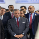 Group of business professionals in suits at a formal event, with a man in a gray suit and red tie center.