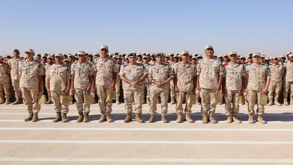image - Center News Network Line of soldiers in desert camouflage uniforms standing in formation on a runway, each holding a small bag, against a clear blue sky.