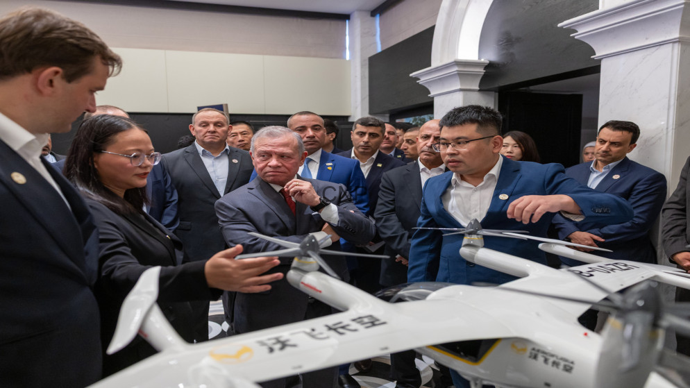 Group of professionals in suits gathered around a white quadcopter drone on display in a showroom.