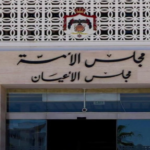 Facade of a government-style building entrance with Arabic signage and a crest above the doors, and glass doors below.