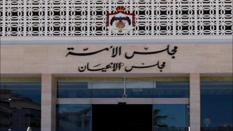 Facade of a government-style building entrance with Arabic signage and a crest above the doors, and glass doors below.