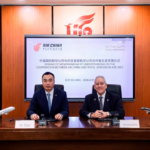 Two executives in suits sign a memorandum at a polished wooden conference table, with model airplanes and a screen showing Air China and Royal Jordanian Airlines logos in the background.