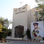 Exterior view of Jordan's Ministry of Interior building with a large portrait of a uniformed officer and Jordanian flags beside the entrance