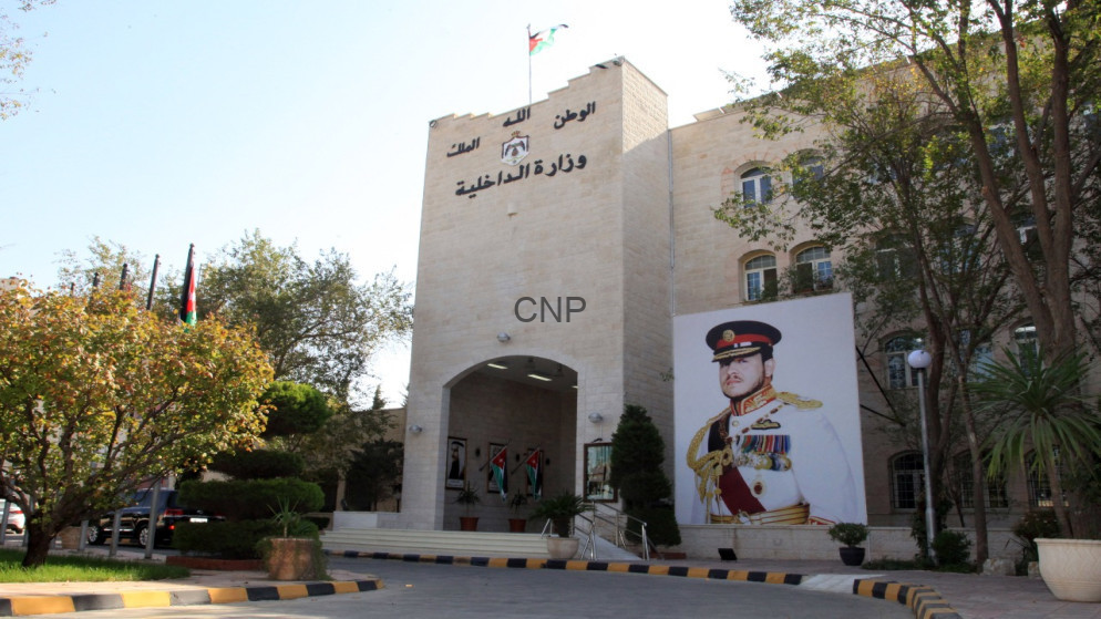 image - Center News Network Exterior view of Jordan's Ministry of Interior building with a large portrait of a uniformed officer and Jordanian flags beside the entrance