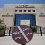 Front view of the Jordan Securities Commission building with a large circular Arabic no-entry sign at the gate and palm trees on both sides.