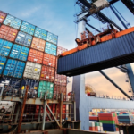 Large stack of colorful shipping containers at a port with a crane lifting a container overhead.