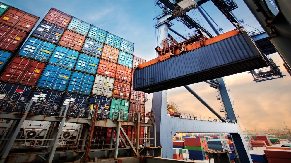 Large stack of colorful shipping containers at a port with a crane lifting a container overhead.