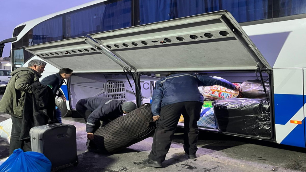 People loading suitcases and bags into the luggage compartment of a white and blue bus.