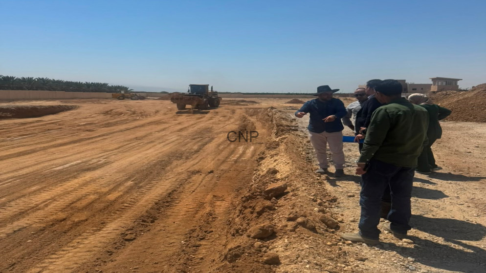 Construction site scene with a bulldozer on a dirt road as a group of workers discuss along the edge of the excavation area.