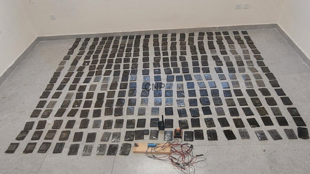 Room with dozens of small black rectangular packages laid out in neat rows on a tiled floor; foreground has cables and testing equipment.