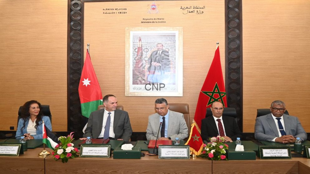 Formal meeting at a conference table with Moroccan and Jordanian flags and a framed portrait behind the speakers.