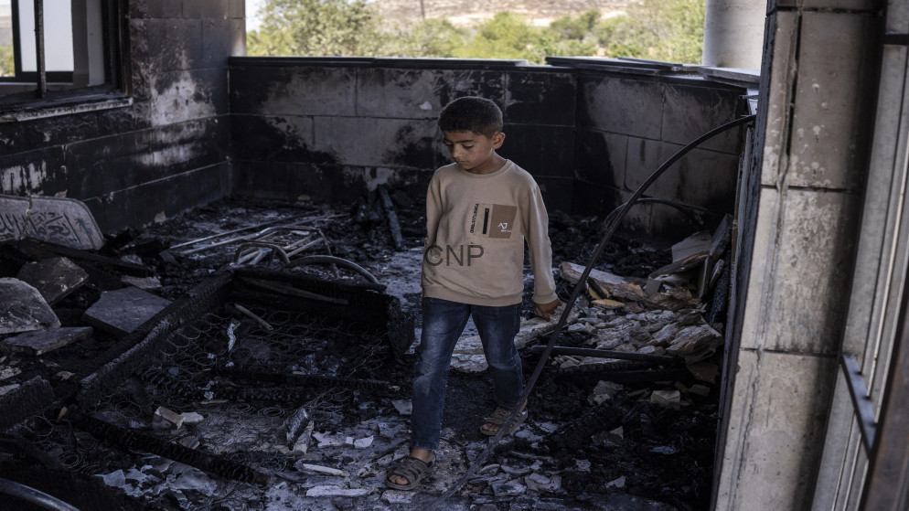 image - Center News Network Boy stands amid charred debris in a burned, ruined room, with blackened walls and scattered rubble around him.