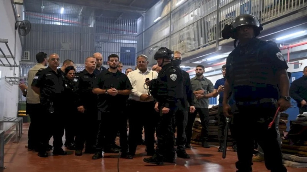 Group of uniformed security officers in a workshop-like setting, listening to a demonstration; two officers in the foreground wear helmets and protective gear.