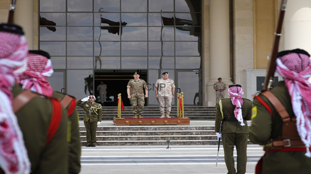Military officers stand on a wooden platform at the top of stone stairs in front of a glass-fronted building during a formal ceremony, with guards in the foreground.