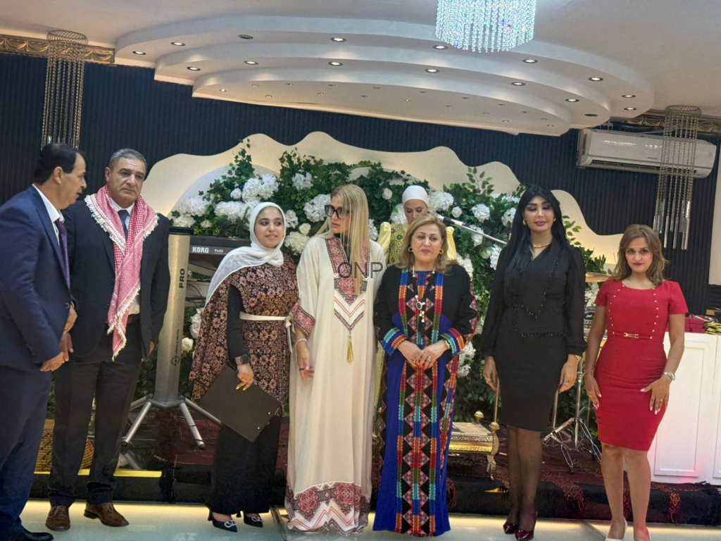 Group of seven dressed in formal and traditional attire posing on a decorated stage with white flowers.