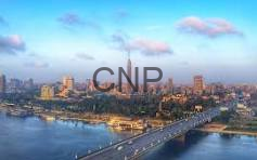 Aerial view of a coastal city with a long bridge across a bay and a dense skyline under a blue sky with clouds; watermark 'CNP'.