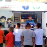 Police officer in a mobile outreach van addressing a group of children outdoors.