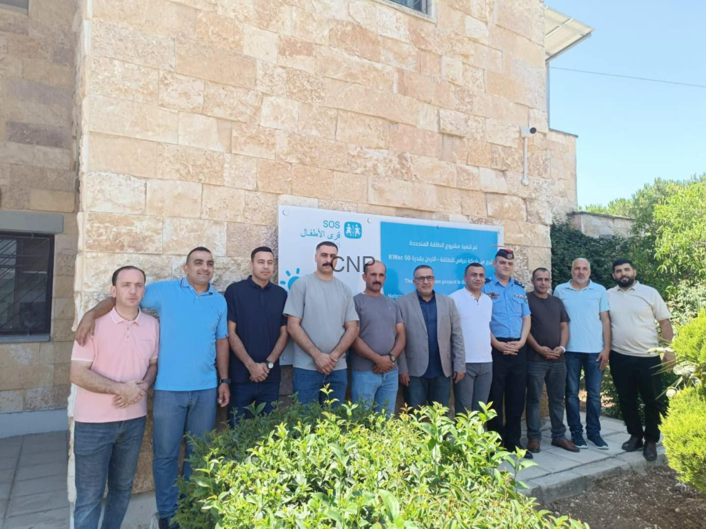 Twelve men standing in a row outside a stone building, next to a blue project banner.