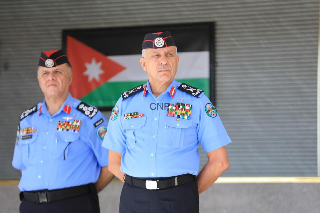 image - Center News Network Two Jordanian security officers in ceremonial blue uniforms with medals, standing in front of a Jordanian flag.