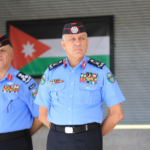 Two Jordanian security officers in ceremonial blue uniforms with medals, standing in front of a Jordanian flag.