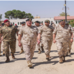 A squad of soldiers in desert camouflage uniforms marching toward the camera on a sunny day.