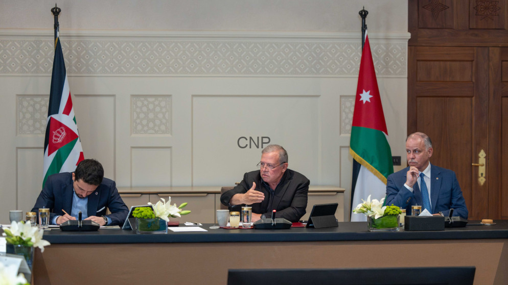 image - Center News Network Three men sit at a conference table with Jordanian flags on either side; center man speaks while the others listen.