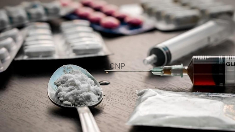 image - Center News Network Spoon with white powder and a syringe on a table, with pill blister packs in the background, implying drug use.