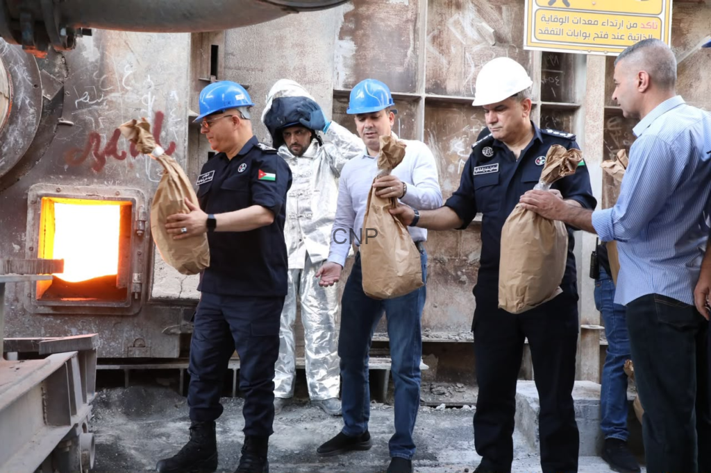 Group of workers in hard hats standing near a furnace, handing out brown paper bags to each other.