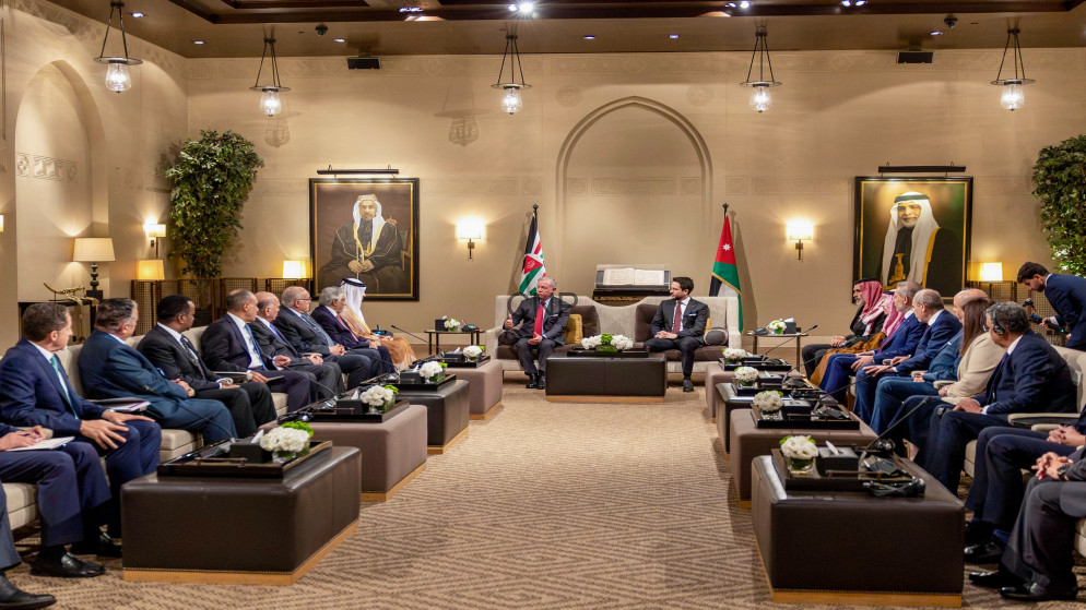 Diplomatic meeting in a beige, opulent room with two leaders seated center, flags behind them, and delegates on both sides.