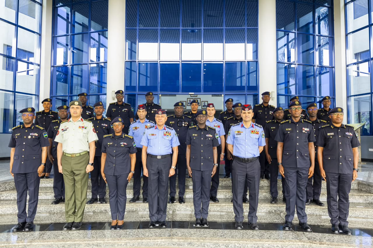 Group of uniformed military officers posing for a formal photo on building steps outside a glass-fronted entrance.