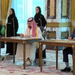 Bilateral signing ceremony between Pakistan and Saudi Arabia with officials signing documents at desks, flanked by flag-bearing aides in an ornate room.
