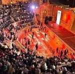 Large crowd gathered around a nighttime outdoor stage with red lights, watching a performance.