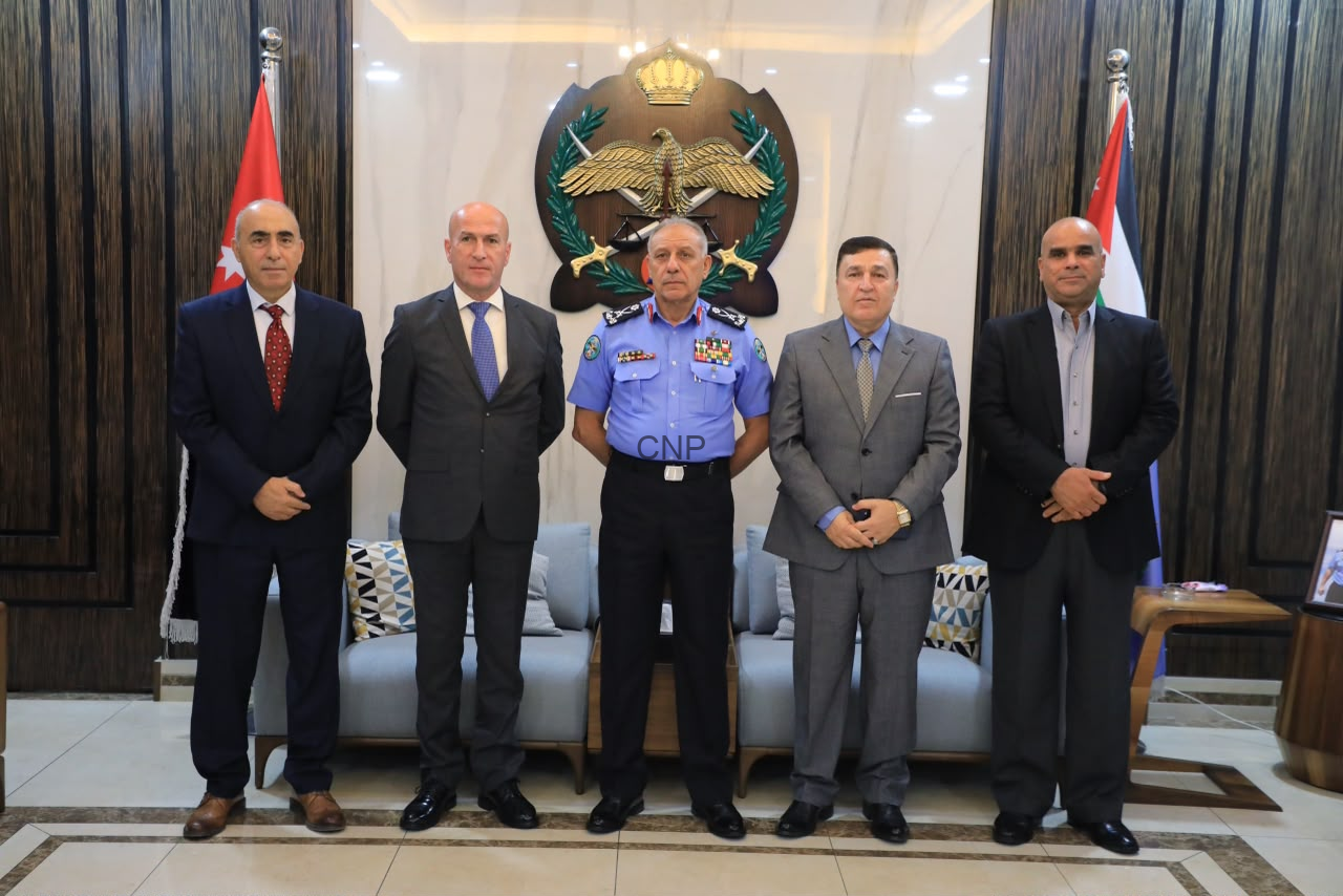 image - Center News Network Five men in formal attire pose for a group photo in a government lobby, center officer in blue uniform with medals, emblem and flags in the background.