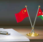Two crossed flags (China and Palestine) on a desk beside a notebook and pen, with a CNPC logo in the background, suggesting a signing or meeting.