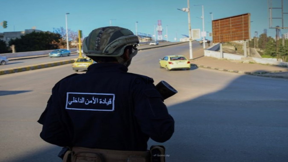 image - Center News Network Security officer in helmet and dark uniform seen from behind, standing at a road junction with cars in the distance.