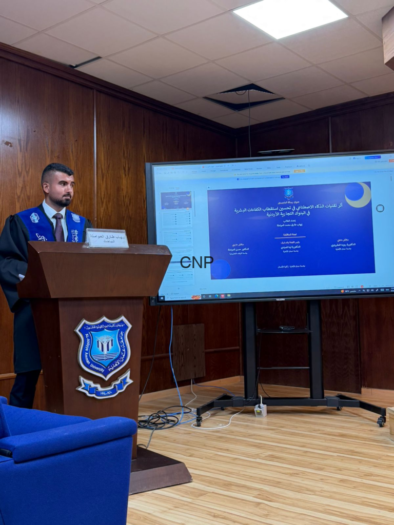 Male lecturer in a blue academic gown stands at a wooden podium with a university emblem, delivering a presentation as a large screen shows a blue slide.