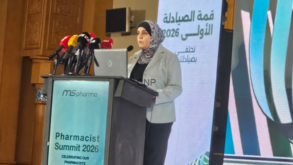 image - Center News Network Woman in a gray blazer speaks at a podium with multiple microphones during the Pharmacist Summit 2026.