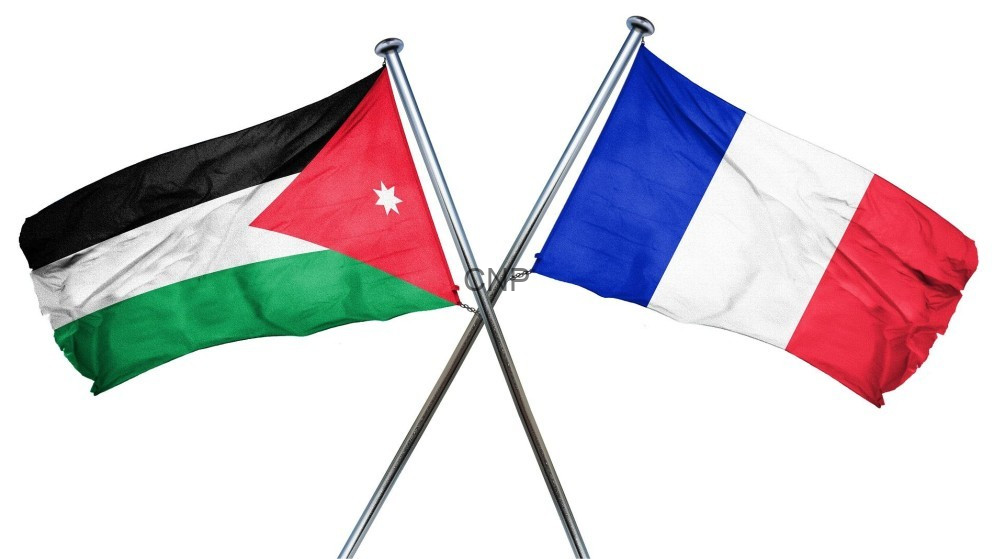 image - Center News Network Two crossed flagpoles display the Jordanian flag on the left and the French flag on the right, symbolizing a flag display or diplomacy.