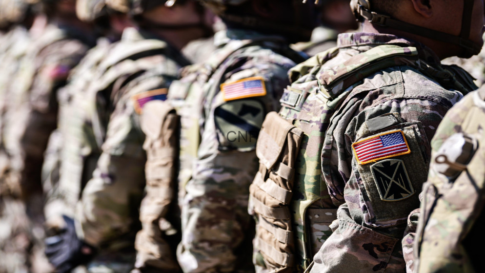 Line of soldiers in camouflage gear with American flag patches, standing at attention.